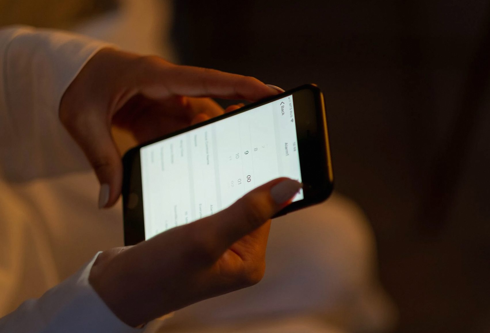 スマートフォンでアラームを設定する手のクローズアップ。夜間の使用とテクノロジーの操作を表しています。